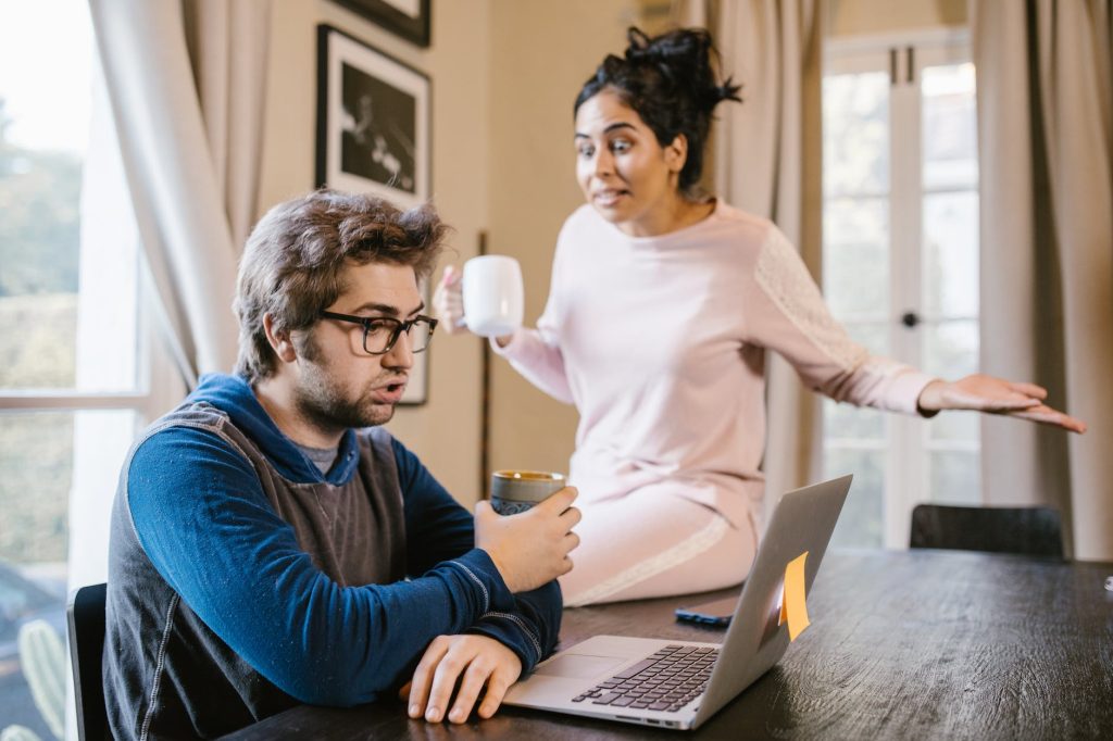 a man sitting in front of a laptop beside an upset woman: Wasting Your Time in a Relationship