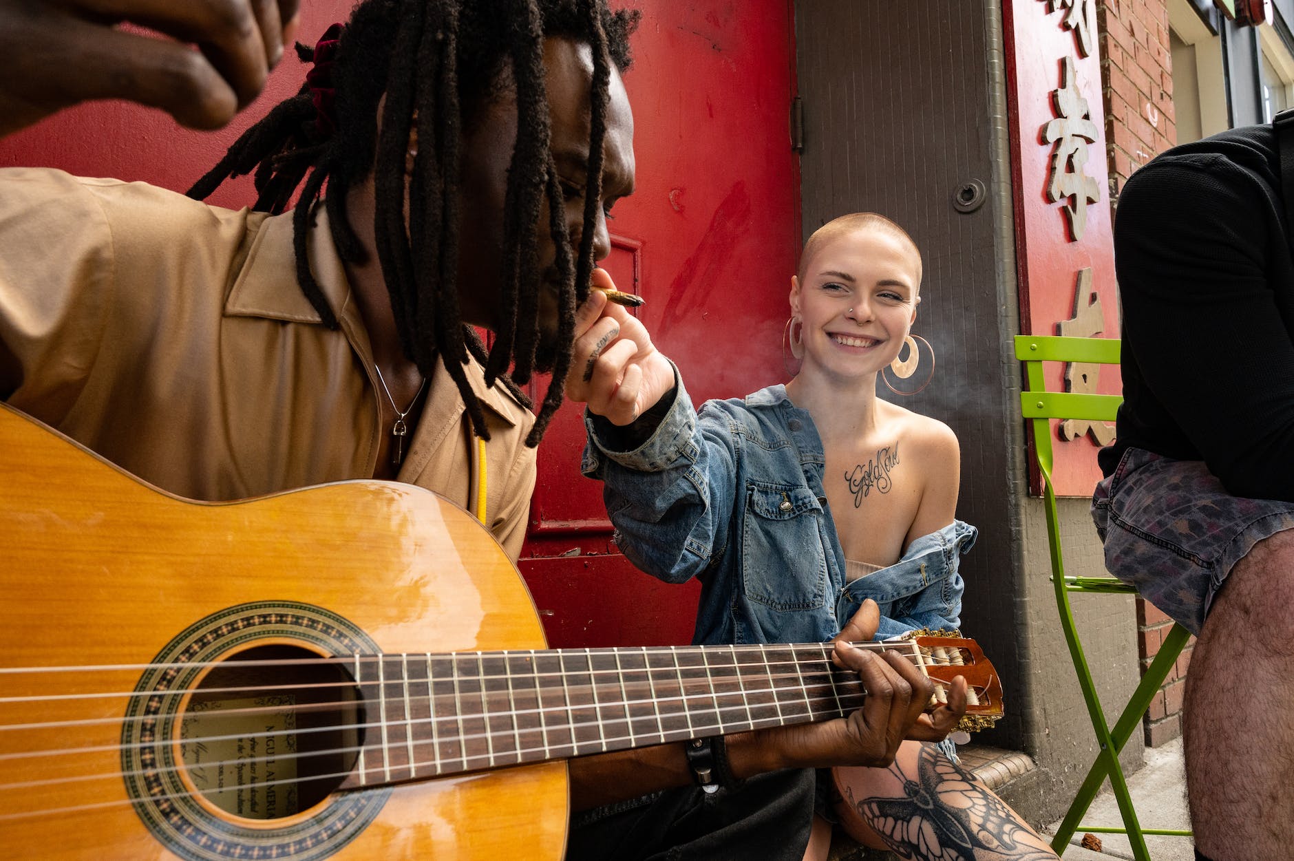 man and woman sitting on sidewalk and playing music and trying to quit smoking