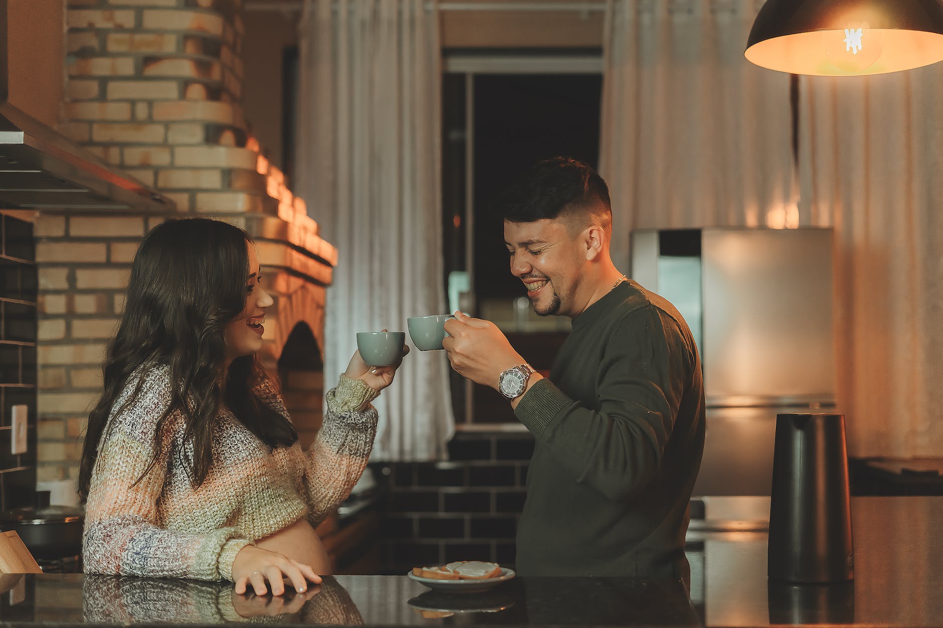 man and pregnant woman laughing at a kitchen holding coffee cups