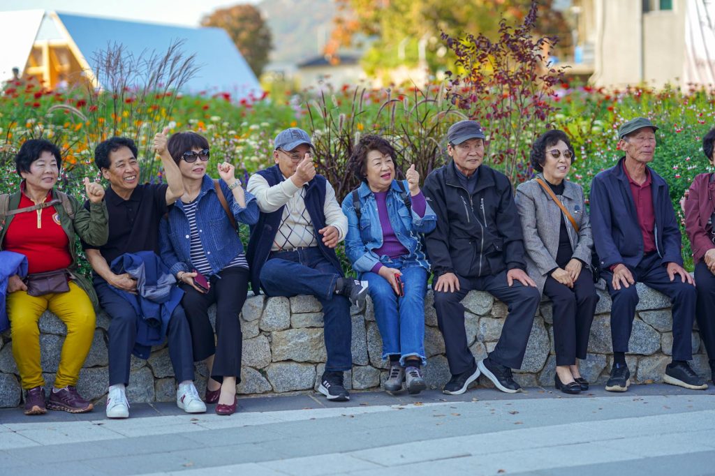 group of elderly people sitting on a stone wall by the sidewalk