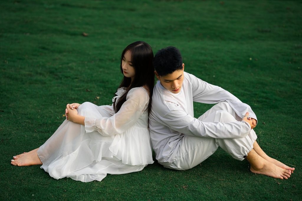 woman in white dress and man in white clothes sitting on grass