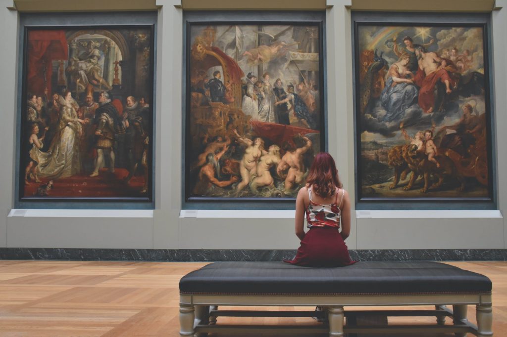 woman sitting on ottoman in front of three paintings: Virtual Date Ideas