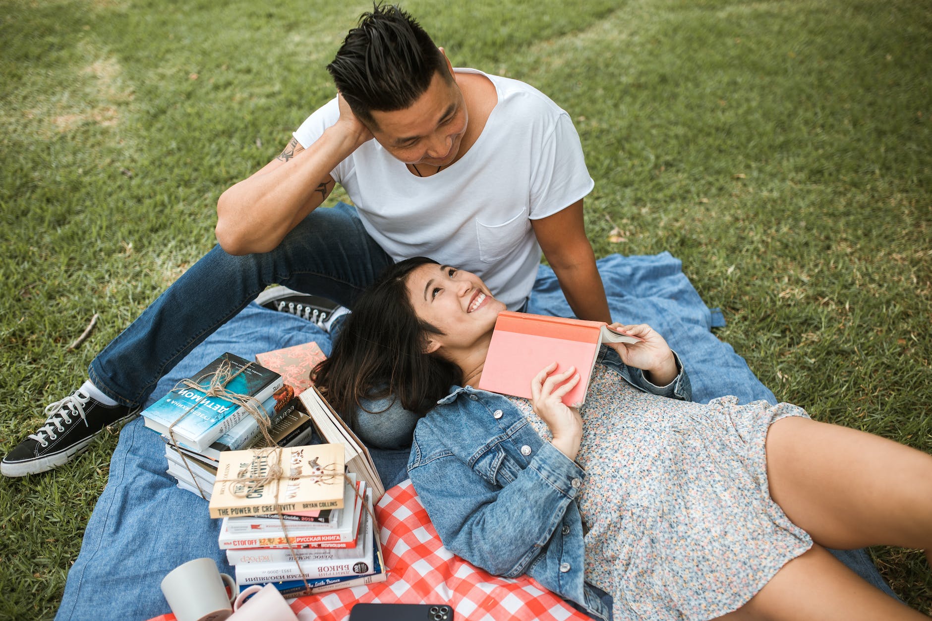 woman in floral dress lying beside man and holding a book